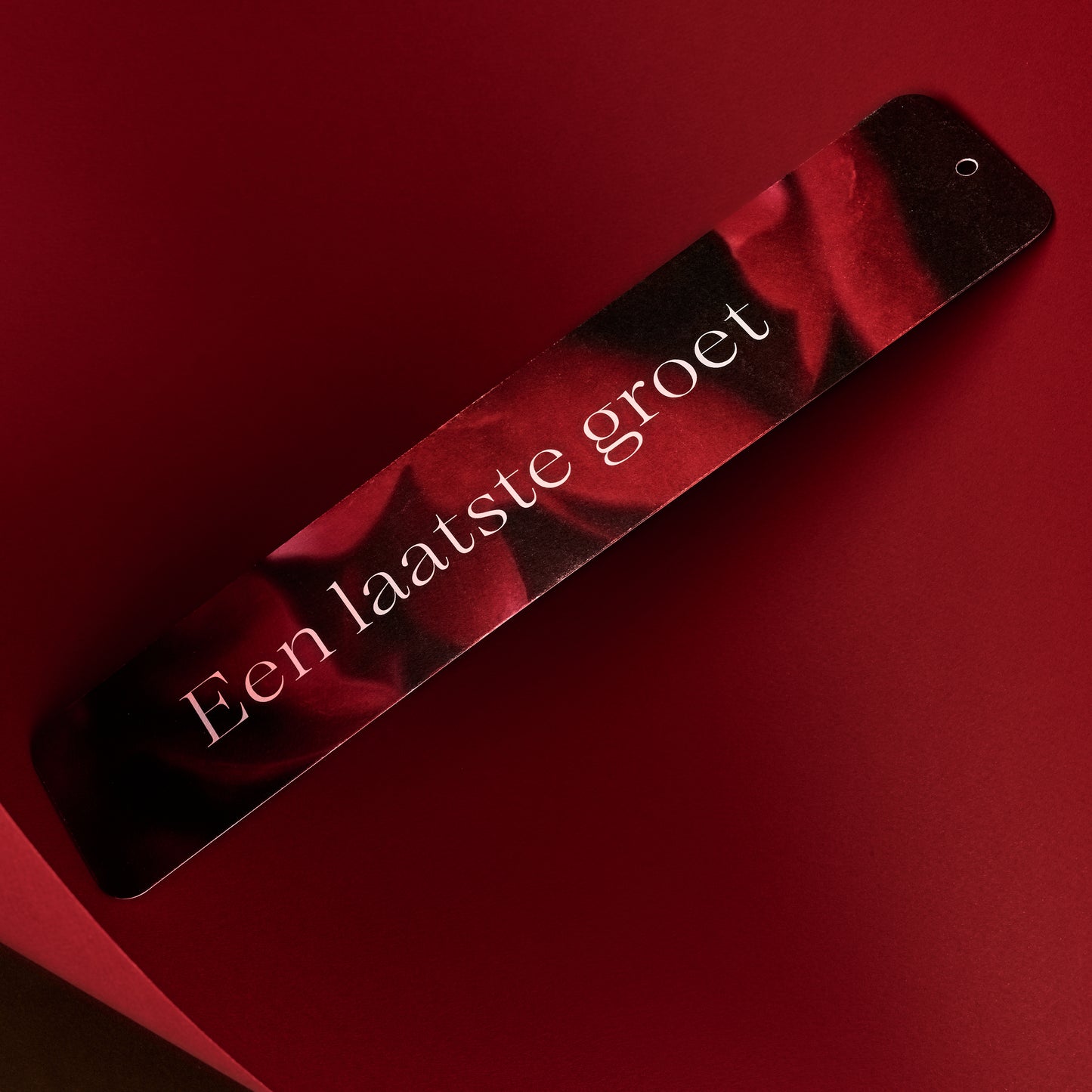 Productfoto van een rouwlint kaart met daarop een roze Pioenroos op een diep rode achtergrond.